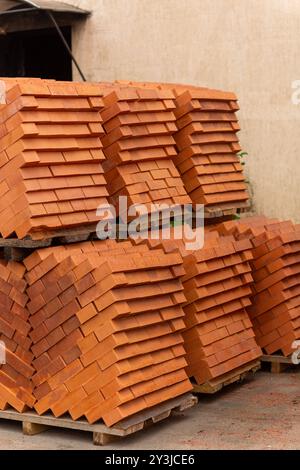 Piles de briques en céramique rouge neuves empilées sur des palettes en bois. Beaucoup de nouveau fond de mur de briques de construction orange et texture. Construction immobilière, Ren Banque D'Images