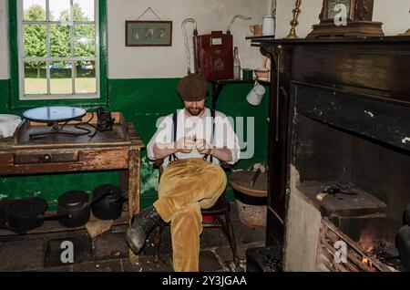 Cultra County Down Northern Ireland septembre 2024 - homme portant un pantalon en velours côtelé et des bretelles assis dans une vieille maison sculptant (blanchissant) un morceau de W. Banque D'Images