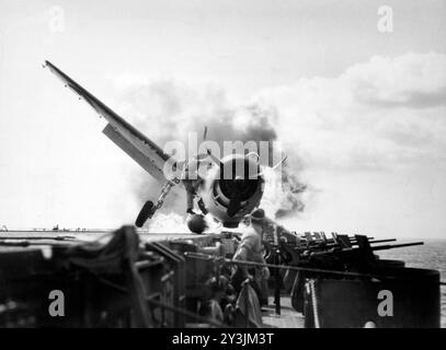 Atterrissage écrasé d'un Grumman F6F-3 Hellcat (numéro 30) du Fighting Squadron 2 (VF-2) à bord du porte-avions USS Enterprise (CV-6), dans la galerie de canons de 20 mm côté bâbord du porte-avions, le 10 novembre 1943. Le lieutenant Walter L. Chewning, Jr., USNR, l'officier de catapulte, est vu grimper sur le côté de l'avion pour aider le pilote à échapper à l'avion en feu. Le pilote, l'enseigne Byron M. Johnson, s'est échappé sans blessure grave. L'Enterprise était alors en route pour soutenir l'opération Gilberts. Notez le réservoir de carburant ventral rompu de l'avion. Photo de l'US Navy. Banque D'Images