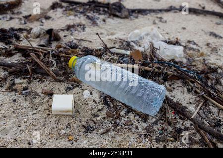 Une plage polluée sur Ko Samui, en Thaïlande, avec des débris de plastique, dont une bouteille et des composants électroniques jetés dispersés sur le sable Banque D'Images