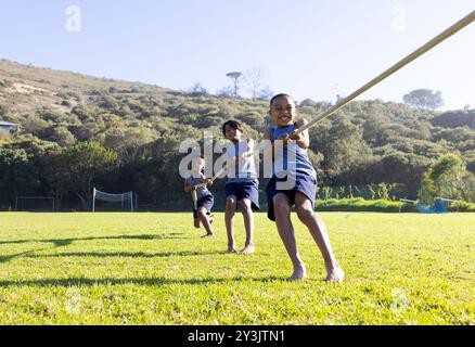 Jouant au remorqueur de guerre, trois garçons multiraciaux s'amusant à l'extérieur sur le terrain de l'école Banque D'Images