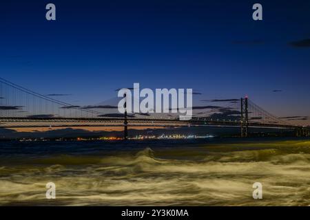 Vue sur le pont ferroviaire du Forth contre Un coucher de soleil avec le Queensferry Crossing Bridge en arrière-plan et les vagues de la rivière Forth au premier plan Banque D'Images