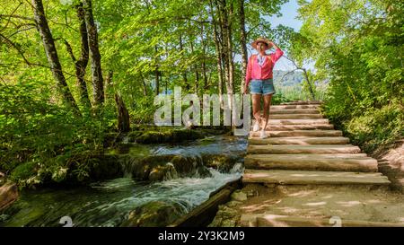 Se promener dans une végétation luxuriante, un voyageur profite de la beauté sereine des lacs de Plitvice. Le soleil filtre à travers les arbres, éclairant la nature vibrante le long des sentiers en bois par l'eau qui coule. Banque D'Images