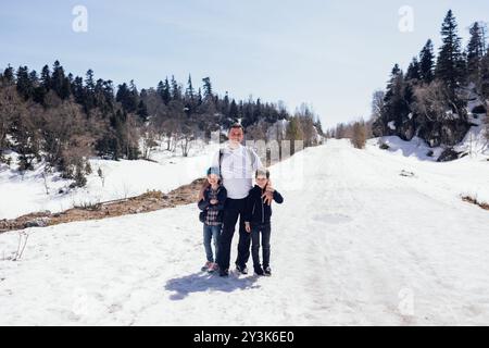 Un jeune homme serre ses petits enfants dans ses bras contre un paysage enneigé. Une famille heureuse est en vacances dans les montagnes. Le père attrayant avec son daug Banque D'Images