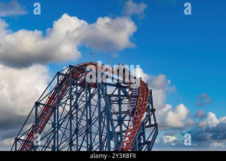 Des montagnes russes palpitantes montant une piste escarpée sur fond de nuages moelleux et d'un ciel bleu vif. Le coaster est rempli de cavalier excité Banque D'Images