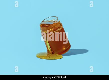 Pot au miel minimaliste sur une table bleue. Égoutter le miel d'un pot en verre directement sur la table Banque D'Images