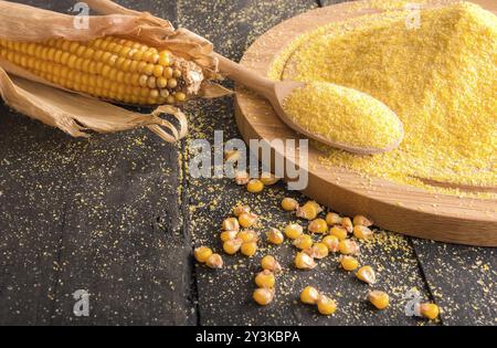 Image de thème des ingrédients alimentaires avec un épi de maïs, des grains et de la farine de maïs sur une trancheuse en bois et une cuillère, sur une table en bois rustique Banque D'Images