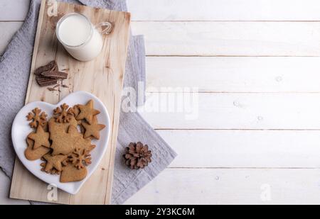 Table de petit déjeuner de Noël avec des biscuits en pain d'épices sur une assiette en forme de coeur, chocolat et lait chaud, sur un plateau en bois, sur une table en bois blanc Banque D'Images