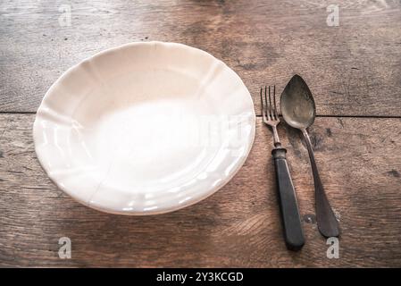 Image rétro avec une vieille assiette fissurée et une fourchette rouillée et une cuillère sur une table en bois. Idéal comme cadre ou arrière-plan avec espace de copie Banque D'Images