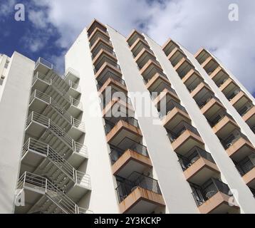 Vue de détail inclinée d'un ancien immeuble d'appartements en béton blanc des années 1960 avec marches et balcons contre le ciel bleu et les nuages Banque D'Images