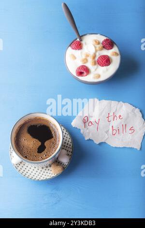 Petit-déjeuner léger composé de café arabe et un bol de yogourt avec des céréales et des fruits et un morceau de papier avec le message de payer les factures, sur fond bleu, ta Banque D'Images