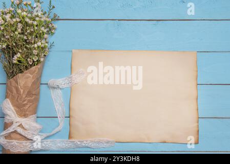 Mise à plat avec l'image de vierge du papier et un bouquet de fleurs blanches sur une table en bois bleu Banque D'Images