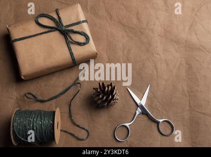 Concept de cadeaux d'emballage avec un cadeau enveloppé dans du papier classique marron, une boule de ficelle verte et des ciseaux sur un fond de cuir marron Banque D'Images