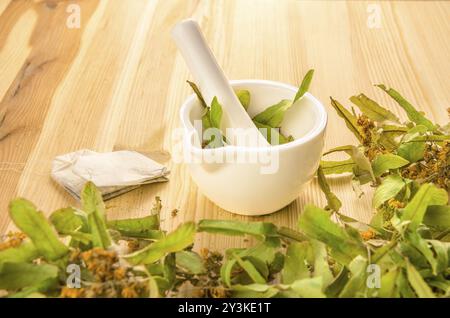 Concept de produits à base de thé naturels et biologiques. Un couple de sachets de thé obtenus en broyant des fleurs de tilleul dans un mortier, sur une table en bois Banque D'Images