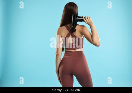 Femme utilisant un masseur à percussion pour soulager les muscles du dos sur fond bleu clair, vue arrière Banque D'Images