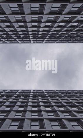 Ciel nuageux entre deux grands immeubles d'appartements modernes avec fenêtres géométriques répétées Banque D'Images