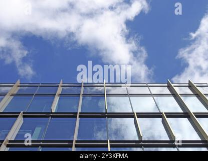 Immeuble de bureaux moderne avec fenêtres en verre réfléchissant reflétant un ciel bleu vif et des nuages blancs Banque D'Images