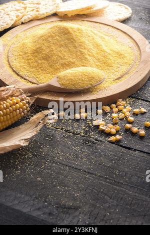 Image verticale avec un tas de farine de maïs sur une planche de bois, un épi de maïs et des grains, gâteaux de maïs soufflés en arrière-plan, sur une table en bois rustique Banque D'Images