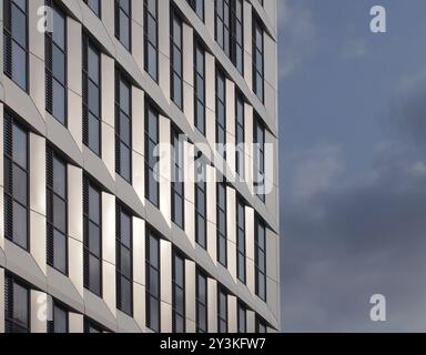 Gros plan détail de perspective de grand immeuble moderne de grande hauteur avec revêtement métallique géométrique et fenêtres sombres à côté d'un ciel nuageux bleu Banque D'Images