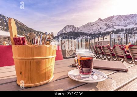 Image avec une tasse de boisson chaude, un menu et un support rustique de couverts, sur une table en bois avec des montagnes en arrière-plan. Photo prise en Autriche Banque D'Images