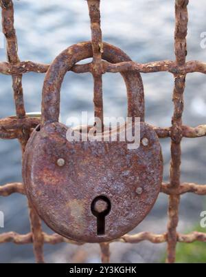 Un gros plan d'un vieux cadenas rouillé sur une clôture en métal corrodé sur un fond extérieur flou Banque D'Images