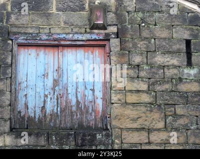 Fenêtre à bord avec volets peints bleus en décomposition avec du bois pourri dans une maison abandonnée abandonnée abandonnée avec des murs en pierre Banque D'Images