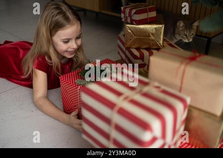 Fille d'âge scolaire en robe rouge ouvrant des cadeaux de Noël à la maison Banque D'Images