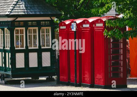 Une scène charmante avec trois cabines téléphoniques rouges emblématiques à côté d'un kiosque vert vintage. Les cabines sont lumineuses et bien entretenues, entourées par l Banque D'Images