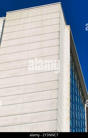 Vue rapprochée d'un coin d'un bâtiment moderne, présentant une façade en béton avec un ciel bleu clair en arrière-plan. Le bâtiment dispose d'un mélange de sm Banque D'Images