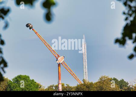 Une attraction palpitante dans un parc d'attractions avec un grand bras oscillant avec une cabine sphérique à l'extrémité, posée contre un ciel bleu clair. A proximité, un grand, slende Banque D'Images