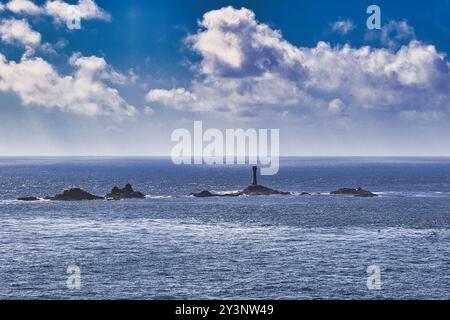 Une vue panoramique d'un phare debout sur une île rocheuse entourée d'eaux bleues calmes sous un ciel partiellement nuageux. Banque D'Images