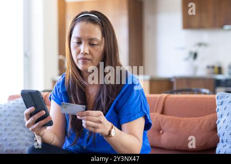 En utilisant un smartphone et en tenant une carte de crédit, femme asiatique effectuant le paiement en ligne à la maison Banque D'Images