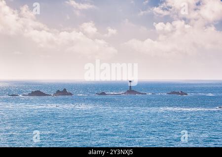 Un paysage marin serein avec un phare lointain sur une île rocheuse, entouré par des eaux bleues calmes et un ciel nuageux. Banque D'Images