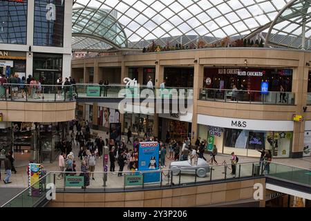 Un centre commercial animé avec plusieurs niveaux, avec un toit en verre. On voit les acheteurs se promener, avec divers magasins visibles, y compris M&S. Là Banque D'Images