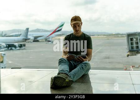 Jeune adulte lisant un guide de voyage en attendant son vol à l'aéroport pour voyager Banque D'Images