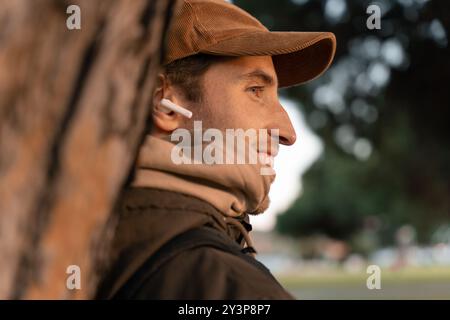 Jeune homme dans les années 30 écoutant de la musique avec des écouteurs dans un parc se relaxant un après-midi d'automne Banque D'Images