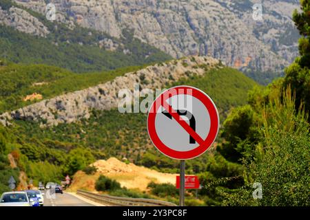 Panneau routier - tourner à gauche est interdit, flèche noire sur fond blanc, barrée en rouge. Aucun virage à gauche contre de belles montagnes. Interdiction routière Banque D'Images