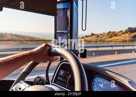 Main tenant le volant d'un camion avec un écran comme rétroviseur et conduisant sur une autoroute, gros plan. Banque D'Images