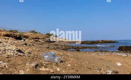 les bouteilles en plastique reposent sur une plage de sable sale, l'océan et la pollution côtière Banque D'Images