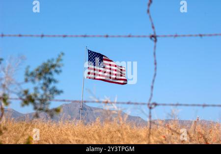 DÉSERT DE SONORAN, ARIZONA, États-Unis : un drapeau américain ondule dans la brise comme vu à travers une clôture de fil barbelé dans le désert de Sonoran en Arizona. Banque D'Images