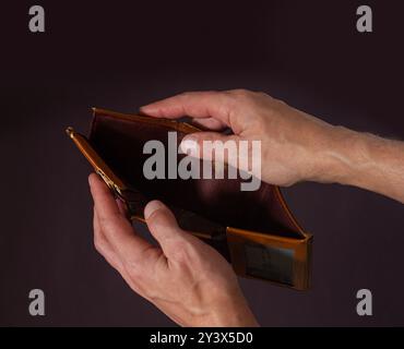 Les mains d'un homme tiennent ouvert un vieux portefeuille vide dans l'obscurité Banque D'Images
