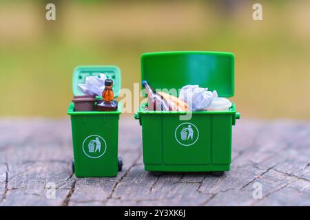 Deux poubelles miniatures vertes remplies de déchets assortis sur une surface en bois, présentant des concepts de recyclage et de gestion des déchets. Banque D'Images