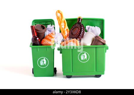 Les bacs de recyclage verts miniatures débordent de divers déchets sur un fond blanc propre. Concept de tri et de gestion des déchets. Banque D'Images