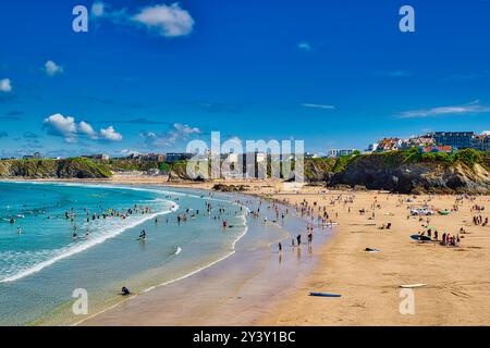 Une scène de plage dynamique avec des gens appréciant le soleil et l'eau. Le rivage sablonneux courbe le long de la côte, avec des falaises en arrière-plan et un bl clair Banque D'Images