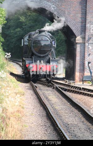 Un vieux moteur de train à vapeur passant sous un pont de chemin de fer. Banque D'Images