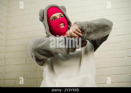 Femme en Balaclava rose dansant contre un mur de briques blanches Banque D'Images