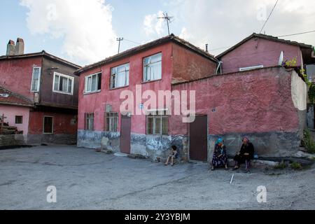 Ankara, Turquie - 13 juin 2022 : deux femmes se reposent au bord de la route, l'une en rose, concentrée sur son téléphone, tandis que l'autre s'appuie contre un mur. Banque D'Images