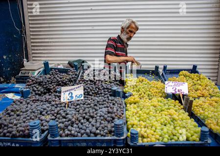 Ankara, Turquie - 13 juin 2022 : scène du marché de rue : un marchand âgé sélectionne soigneusement les fruits, entouré de caisses de raisins mûrs au prix du magasin local Banque D'Images