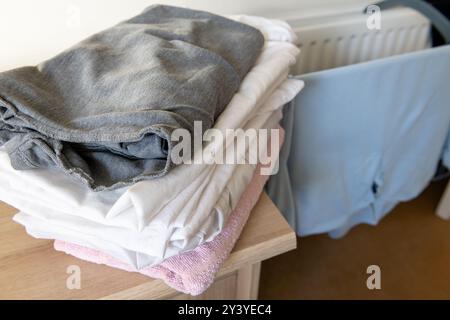 Buanderie maison avec des vêtements lavés séchant sur support par un radiateur et une pile de vêtements séchés pliés. Banque D'Images