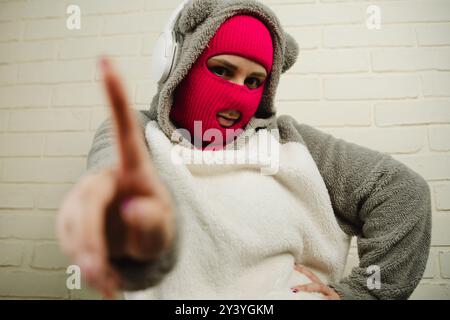 Femme en Balaclava rose dansant contre un mur de briques blanches Banque D'Images